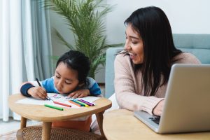 Happy Asian mother work on computer at home with her child - Focus on son face - Family concept